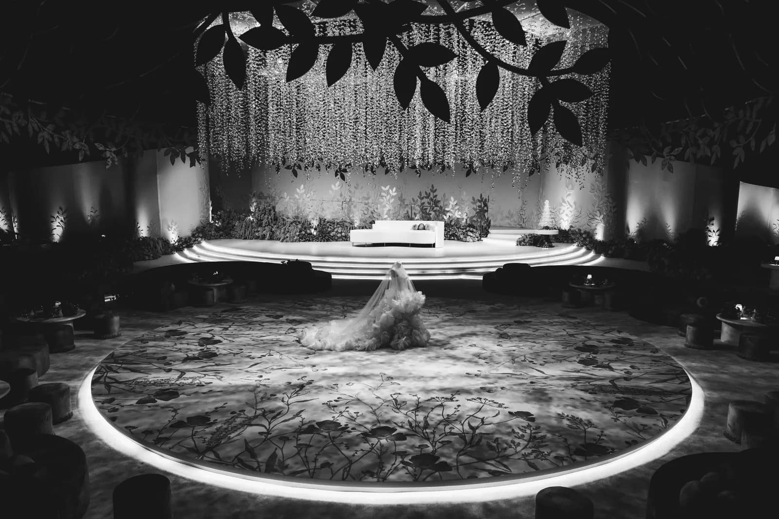 Black-and-white Moements wedding photograph with a bride beneath suspended floral installations
