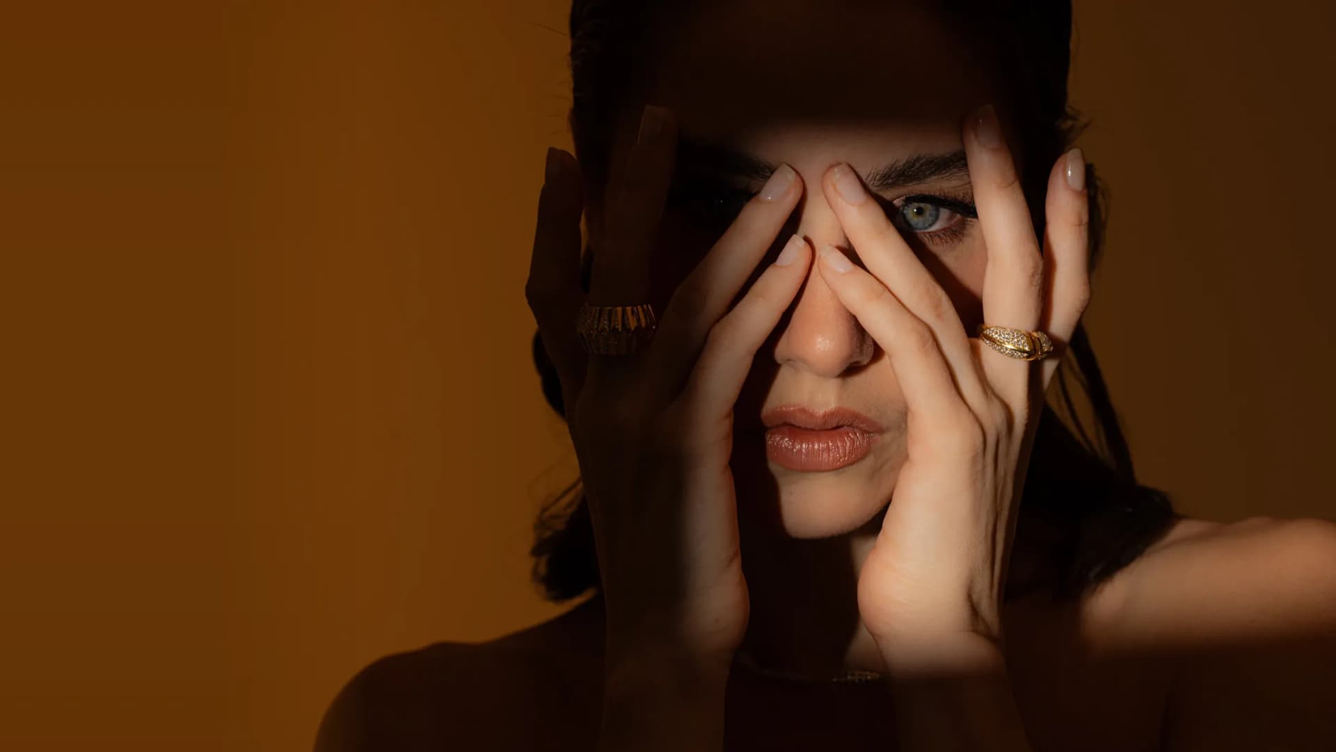 A Dina J Jewelry campaign portrait: a model framing her face with gold rings