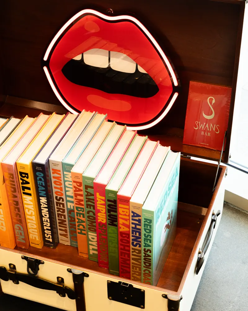 Cities store: a red lips neon sign above travel books in a vintage trunk