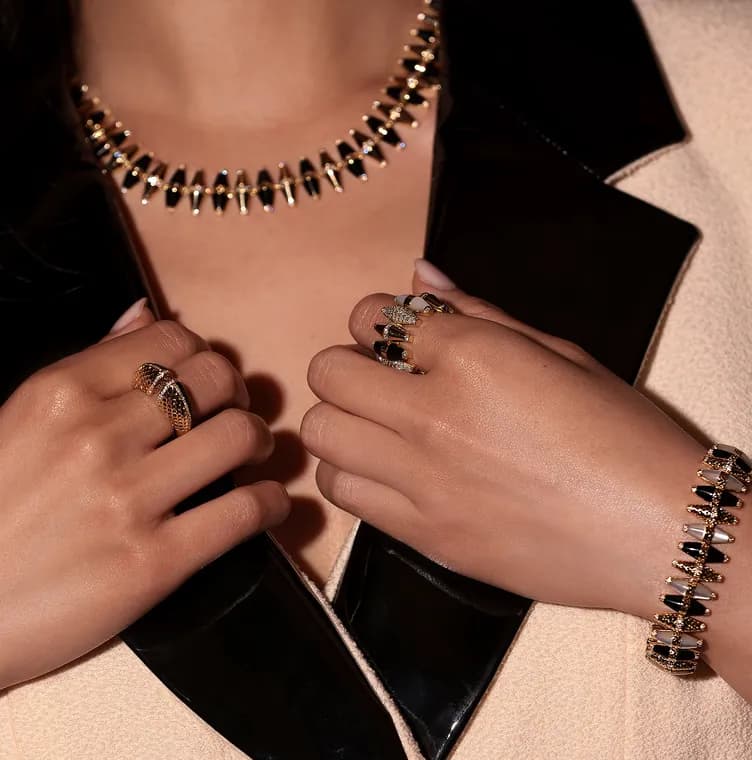 Dina J Jewelry campaign: a gold necklace, rings and bracelet against a cream jacket