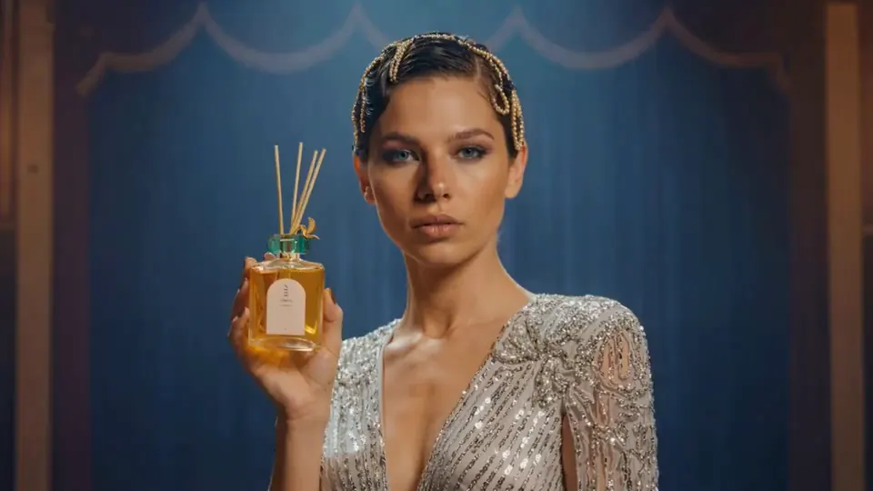Verbleu campaign film: a model holding a reed diffuser against a blue stage curtain