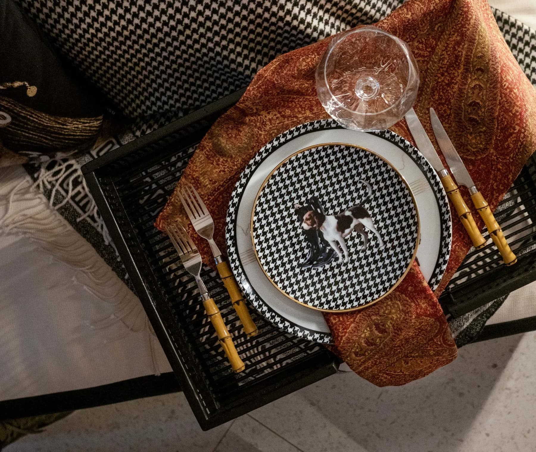 A Vitelli table setting: a houndstooth plate with a hound, bamboo cutlery and a paisley napkin