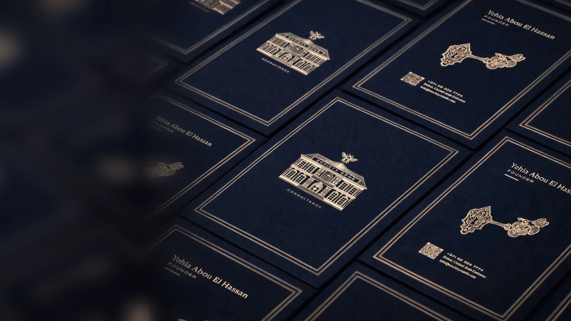 Society Comb business cards in navy with gold foil: the house-and-bee logo and the founder's card with the lock-and-key emblem